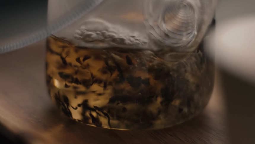Hot water pours into a glass teapot swirling the loose tea leaves as they begin to steep