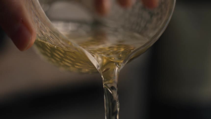 A person pours liquid into a teacup from a glass cup