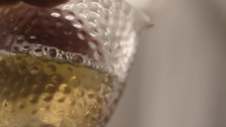 A hand holds a textured glass pitcher filled with a golden liquid