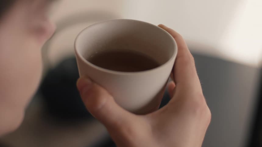 Person holding white cup with dark beverage during moment of consumption