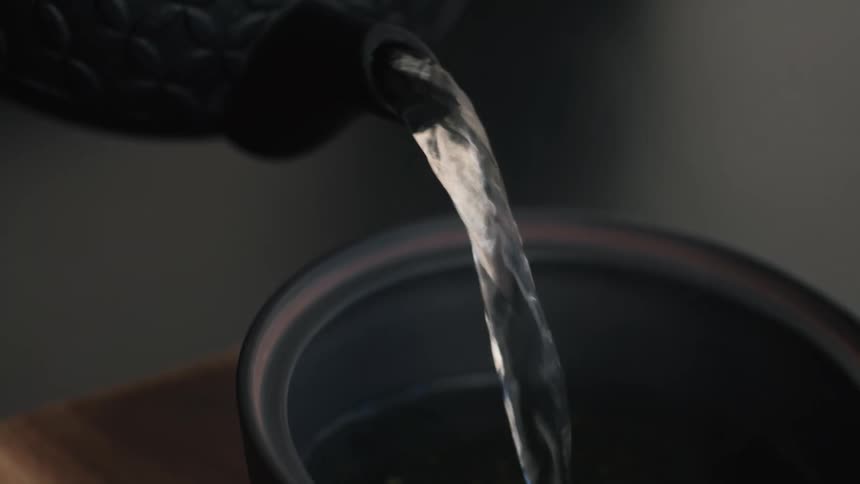 Close up of a person preparing tea in a bowl with warm water from a black kettle