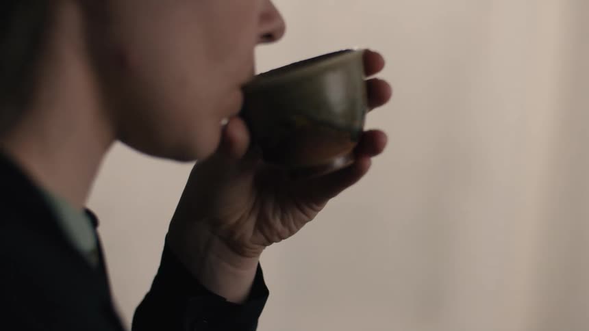 Person holds rustic cup near mouth during hot beverage consumption moment