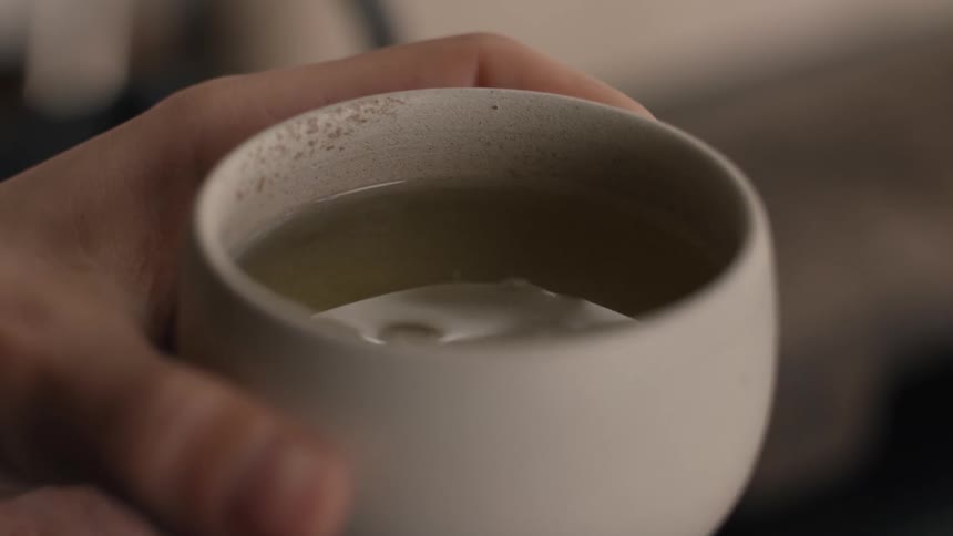 Hand holds white cup with yellowish liquid and suspended particles