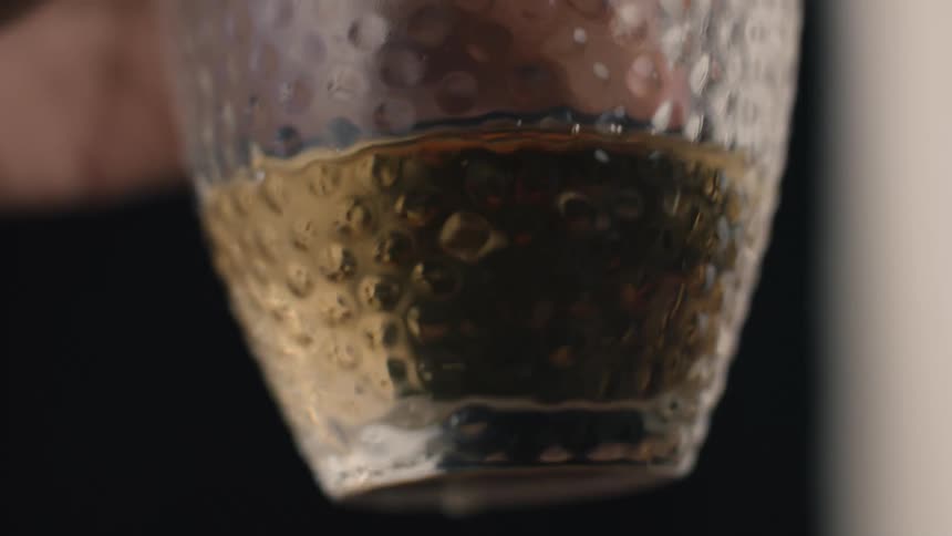 Human hands holding a glass cup containing a yellow beverage indoors