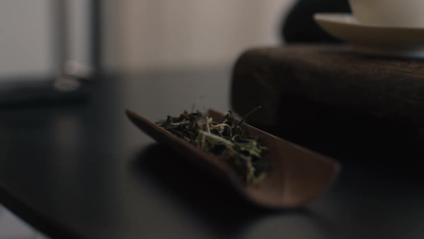 Hand pouring tea leaves into a cup on a table
