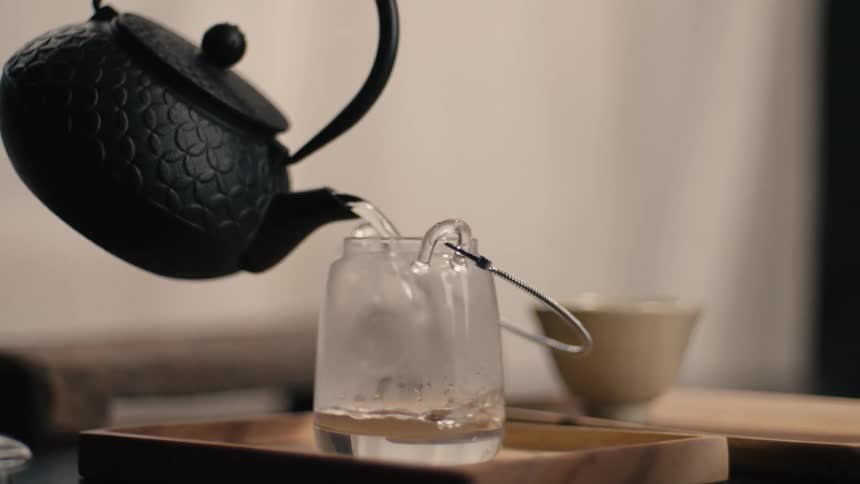 A person pours water from a teapot kettle into a clear glass