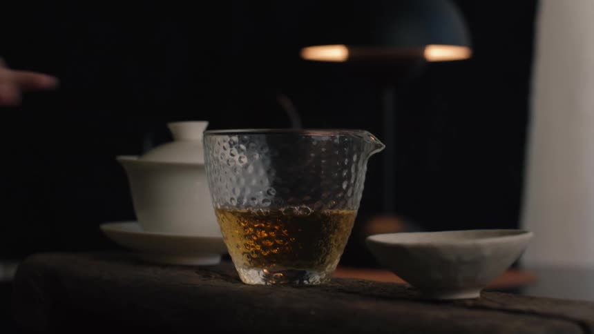 Hand pouring hot tea from a teapot into a textured glass