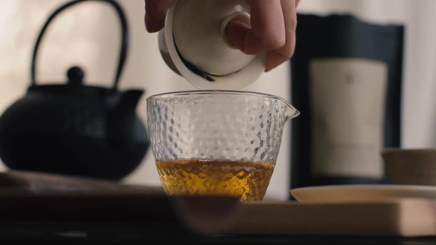 The person fills the glass with tea