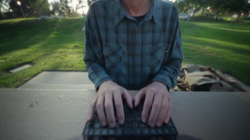 Person typing on portable device at outdoor table in wooded area