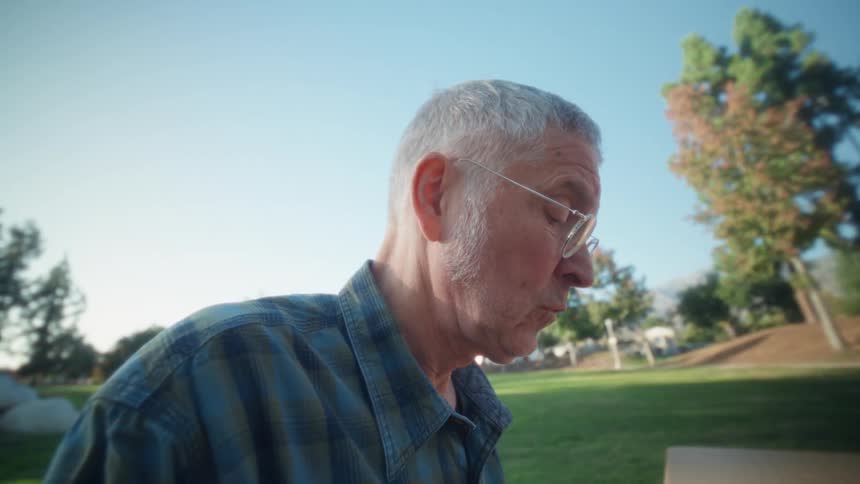 Man sitting outside at a table holding his phone as he types on a computer keyboard