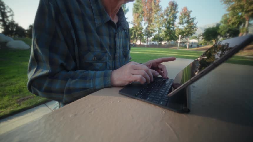 Older adult using keyboard in park with autumn trees under blue sky