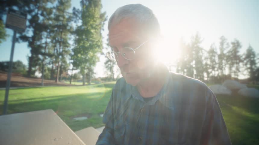 The man in the park is using his tablet and typing