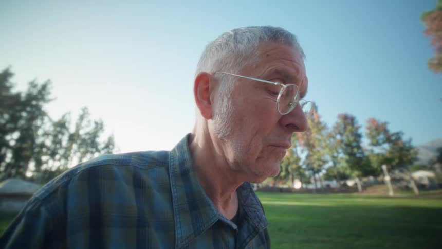 Elderly man using a laptop at a concrete table in an outdoor park