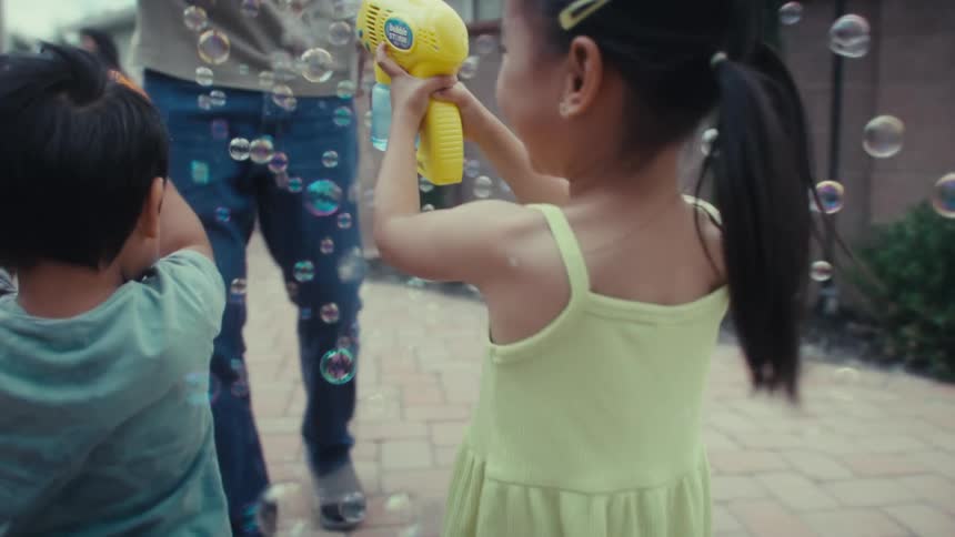 Two kids play with their father using a bubble gun in the backyard at midday with fun and excitement