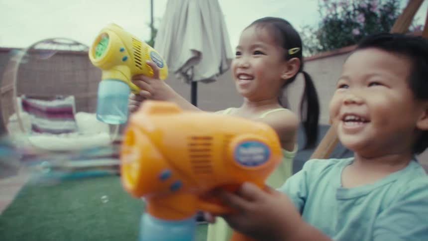 Small boy and small girl playing with bubble toy guns on an outdoor play area during day time