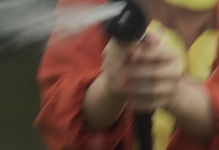 A young boy holds a water hose spraying water while screaming at midday