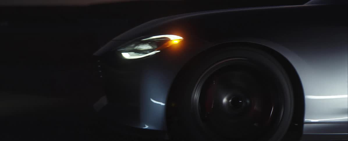 Front side of dark sports car in motion with blurred wheel and lights on at night