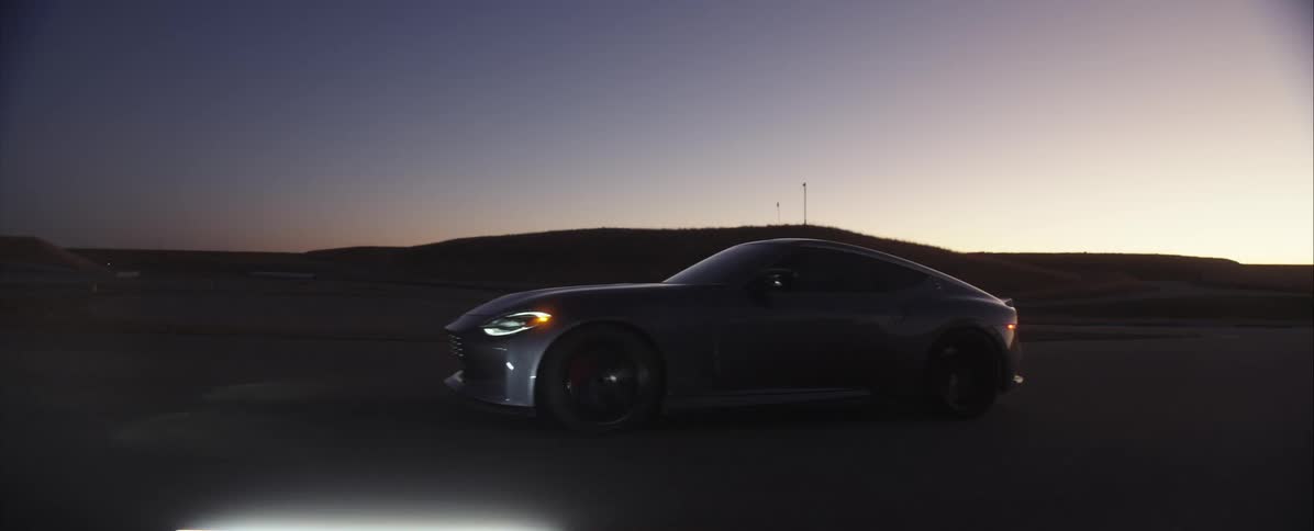Modern sports car driving on paved road at dusk with headlights on