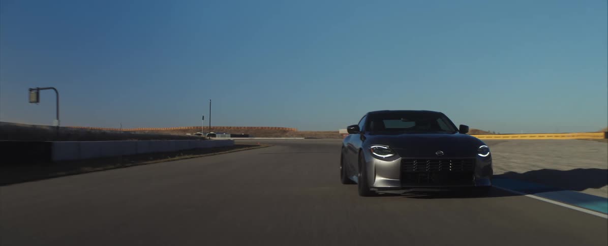 Nissan z sports car driving on paved track with headlights on under blue sky