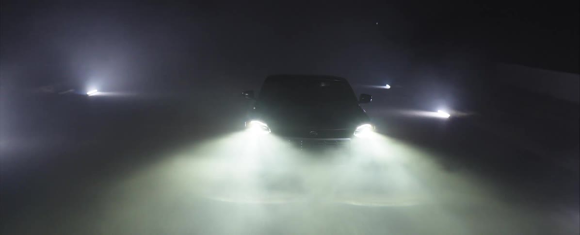 The car is driving in the dark with its headlights on and passing through a patch of fog
