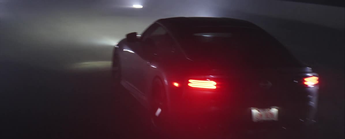 Silver nissan sports car driving on dark road with tail lights on