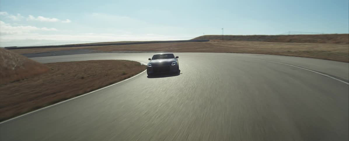 Black sports car driving on track curve surrounded by dry vegetation under sunny sky