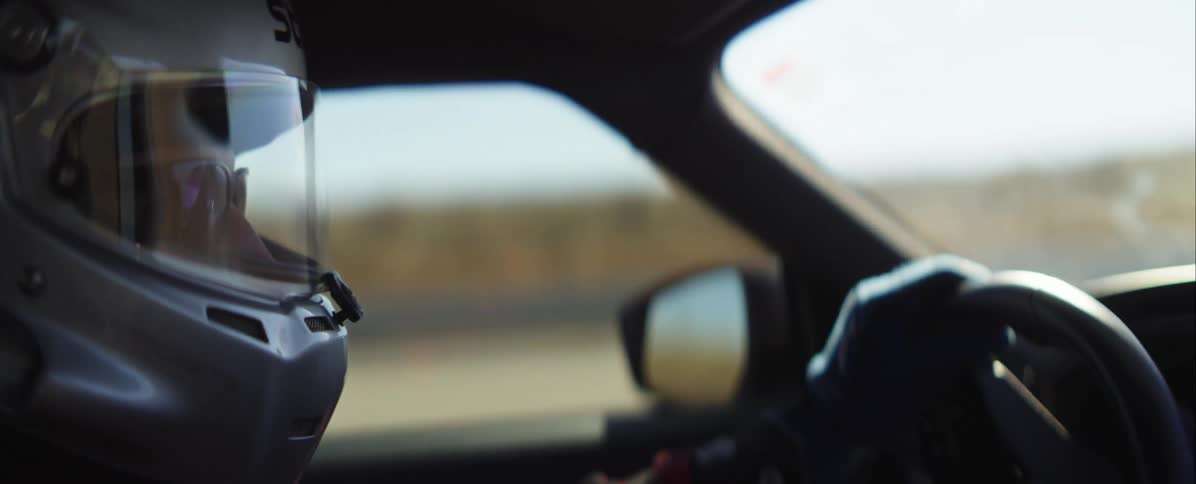 A driver wearing a white racing helmet and blue gloves steers a vehicle on a bright sunny day on an open dry course