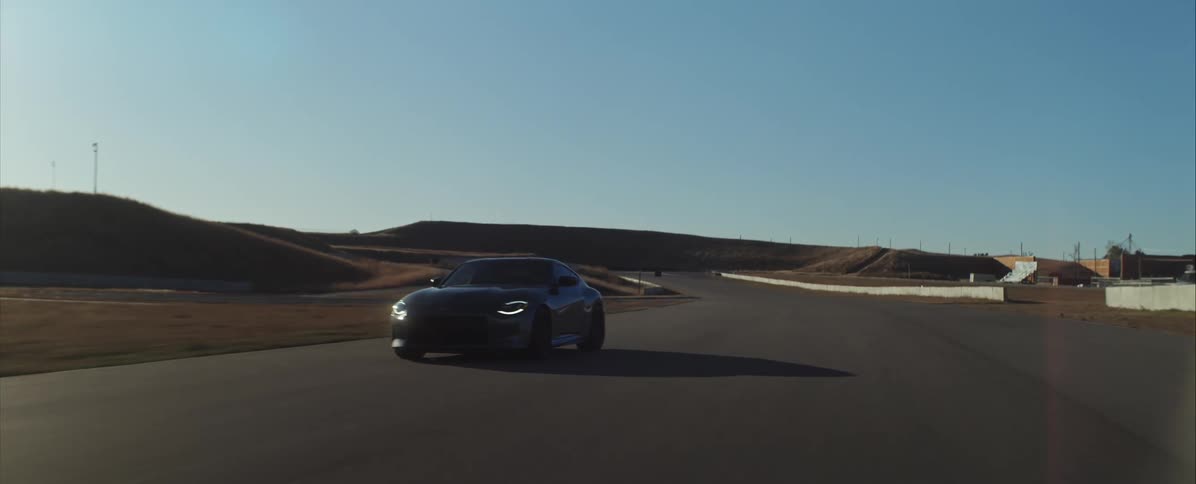 Sports car moving along a straight section of an asphalt track surrounded by hills