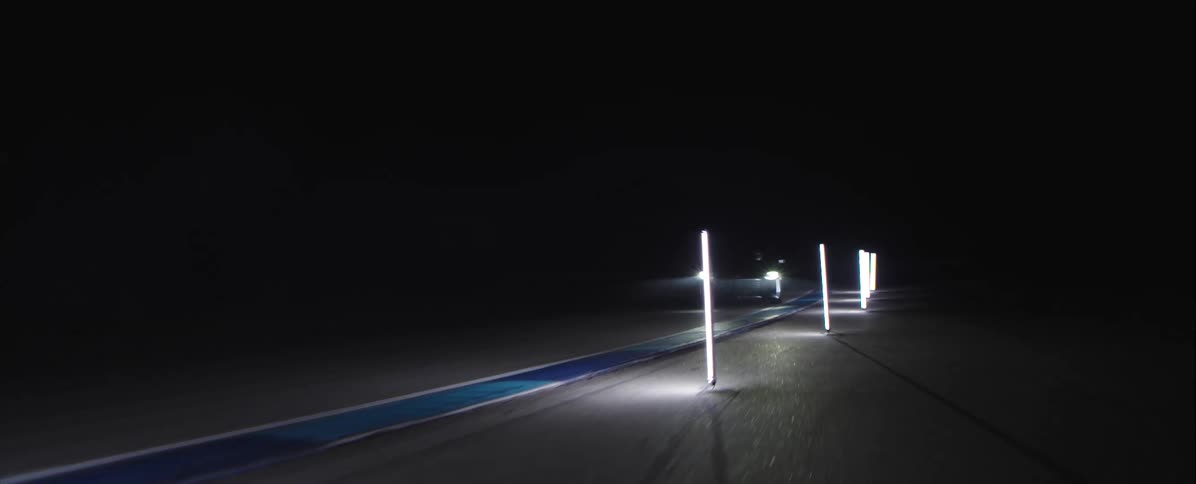 The car is driving beside the tall thin lights that are on the edge of the track