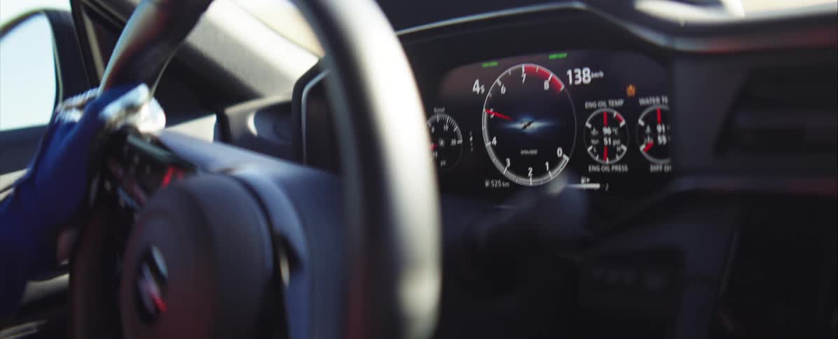 A closeup of a digital car dashboard during a highspeed run with the drivers gloved hands operating the steering wheel as the vehicle shifts gears