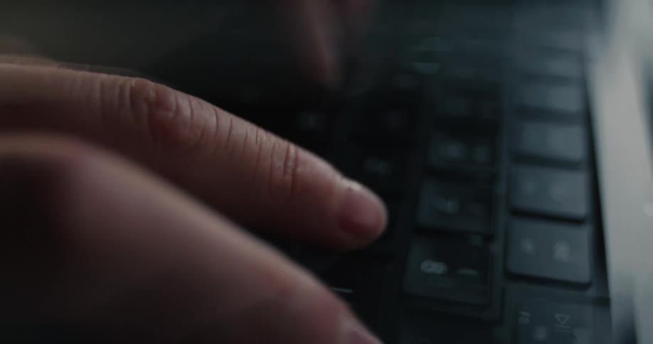 A close view of a womans fingers rapidly typing on the black keyboard of a laptop in a dimly lit setting