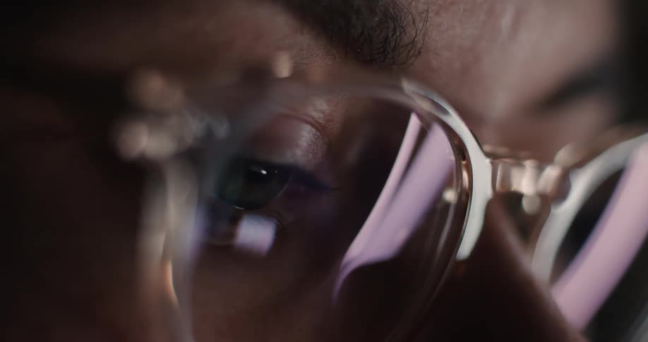 Glasses with colored reflections in a closeup of eyes focused on a screen
