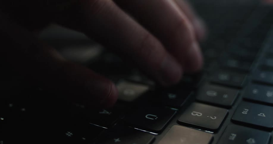 Person typing on keyboard with low lighting and focus on keys and fingers in motion