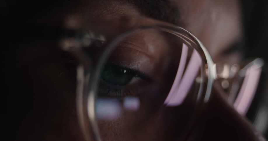 A woman wearing glasses looks at a screen with its light reflecting off the lenses