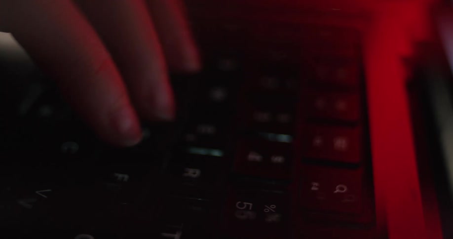 The camera is focused on the hands typing on the keyboard in the darkness