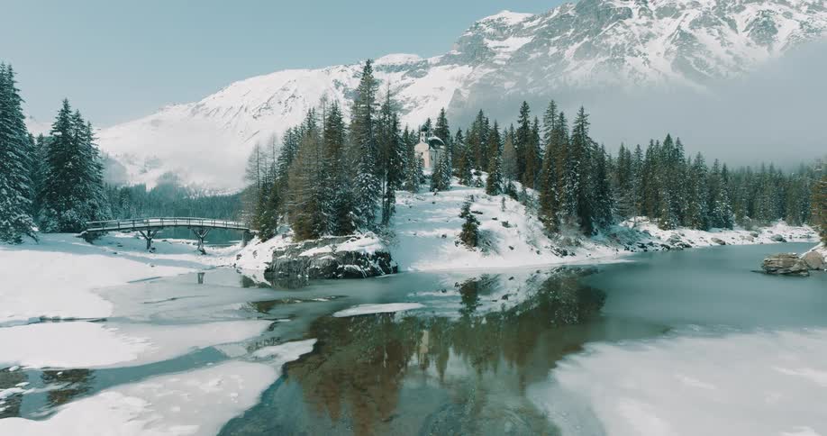 Building on a hill surrounded by trees on the coast at the foot of snow covered mountains