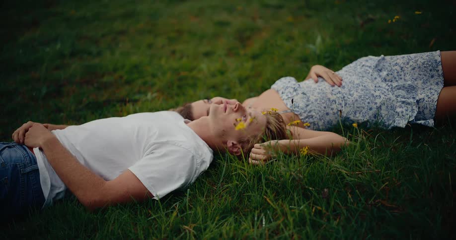 A man and woman are laying on bright green grass looking upwards touching each other