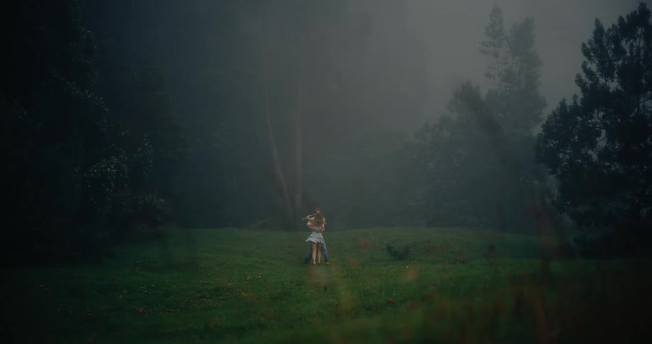 A romantic couple spins joyfully together in a misty open field surrounded by soft fog