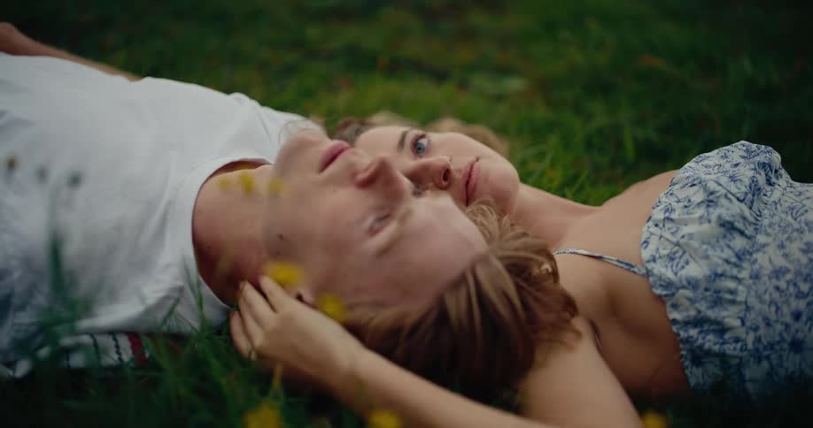 A young man and woman lay together on the grass outside