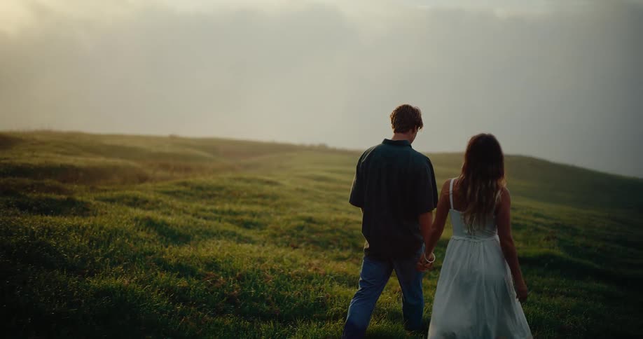 A young couple walking together along a grass field outdoors during daytime