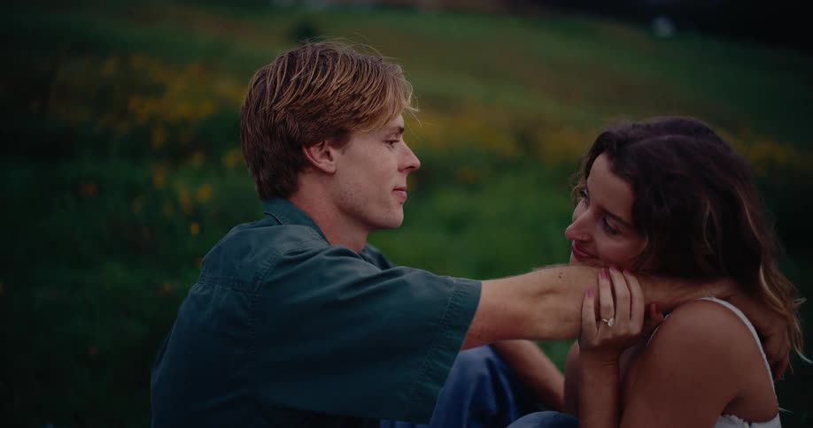 The man and woman sit together hugging in the grass