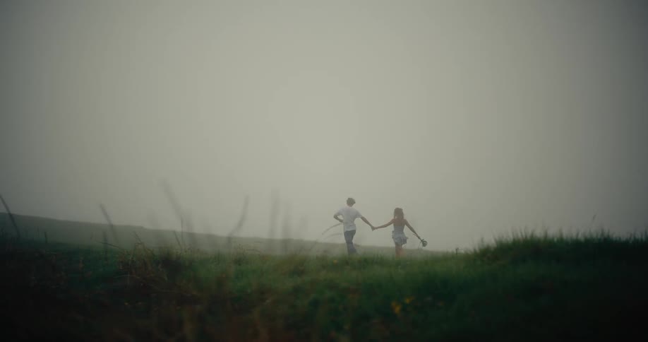 A man and woman running through a grassy field with fog