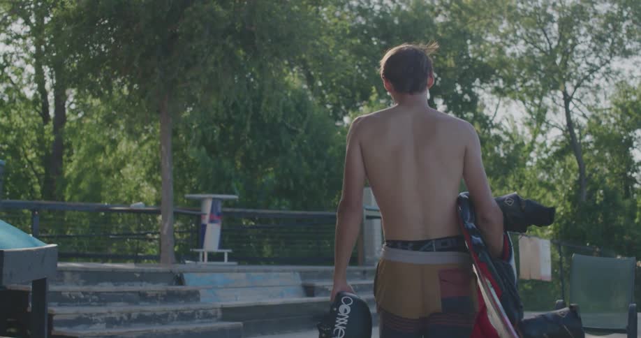 Young man carrying a wakeboard under his arm and a helmet in his hand