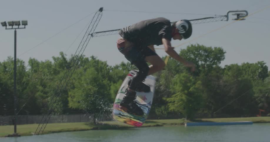Man rides a wakeboard holding a rope as he flies into the air and splashes back down