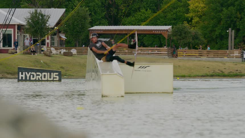 A wakeboarder attempts a jump off a white obstaclerail in a cable park executing an aerial trick before crashing headfirst into the water and creating a massive splash
