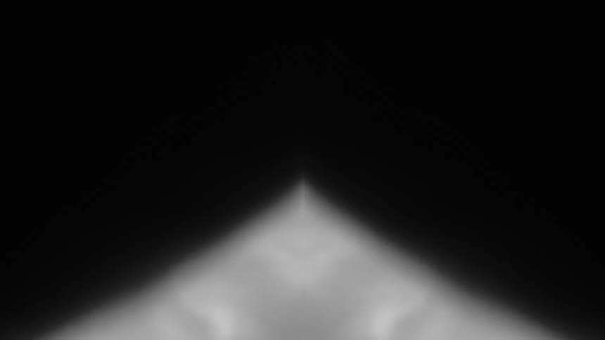 A sharp triangular beam of white light cuts through the heavy darkness revealing a drift of atmospheric fog swirling within its geometric glow