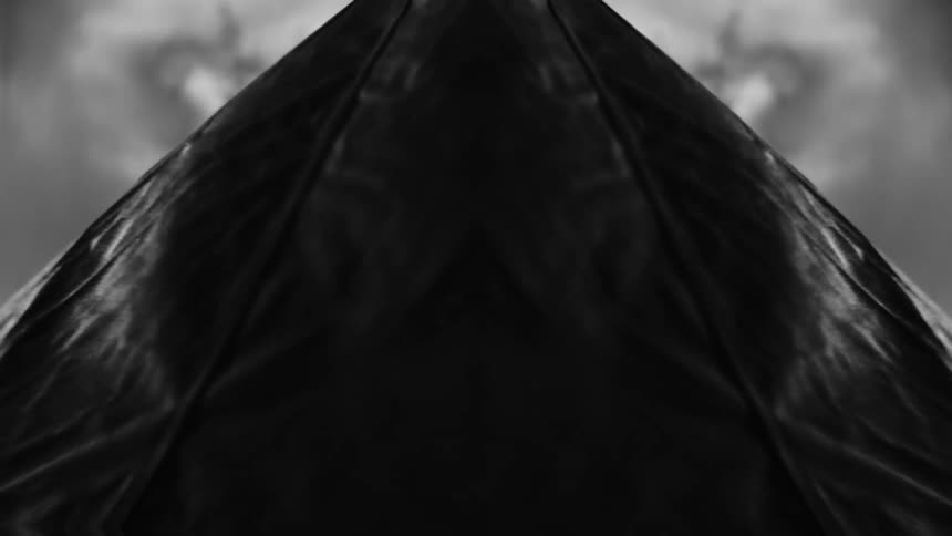 A black and white abstract visual features a slow zoom into a pyramid shape composed of swirling fabric textures against a dark sky