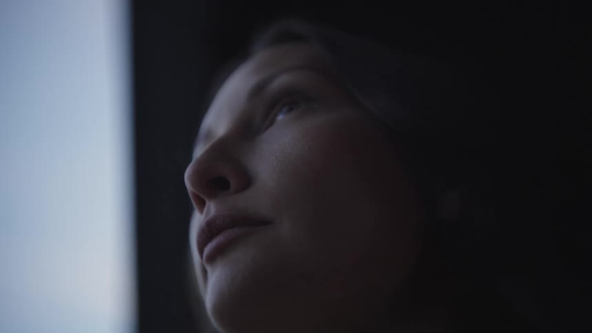 A low angle close view of a thoughtful womans face in the dark softly lit by a bright vertical light source from the left
