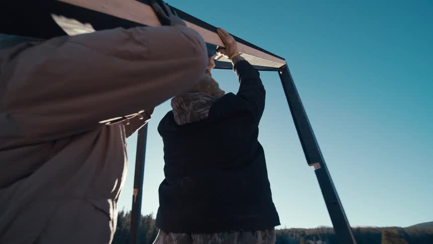 Two people lifting a metal structure in a sunny outdoor area