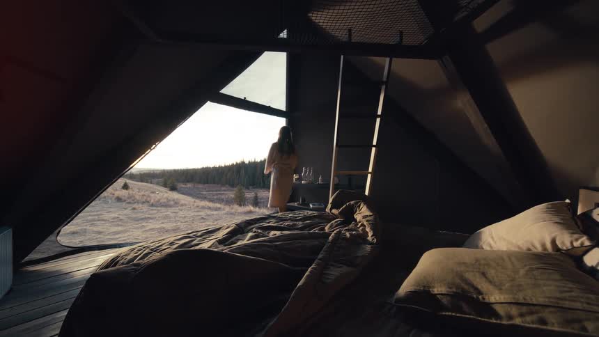 A woman walks through a modern cabin bedroom looking out at a snowy landscape